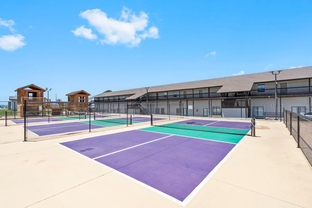 An energetic outdoor space showcasing well-maintained tennis courts and a lively playground set within thoughtfully landscaped grounds. Children and families are visible making the most of the amenities.