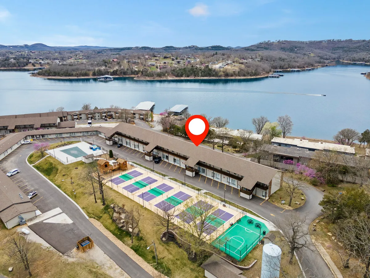 A panoramic exterior view featuring vibrant tennis courts, a scenic lake, and areas for outdoor recreation, all nestled in natural surroundings. The image conveys both activity and tranquility, with the lake hinting at boating and water sports nearby.