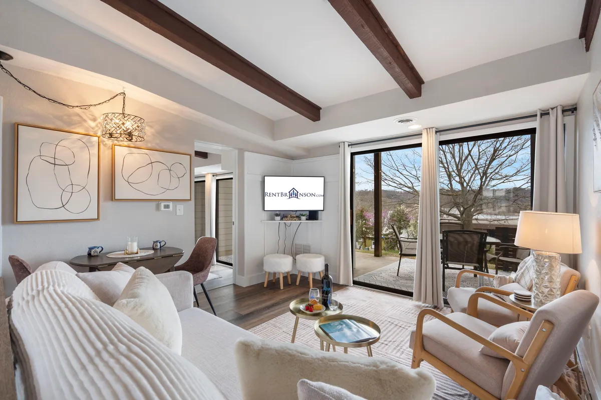 The image showcases a bright, welcoming living and dining area with a plush sofa, a modern dining table set for four, and expansive windows that fill the space with natural light and offer serene views. Tasteful decorative lighting and cozy decor create an inviting atmosphere, ideal for relaxation or quality time together.