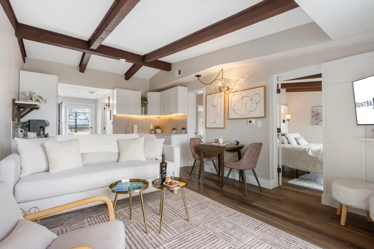 A bright, open-concept living and dining area featuring a plush sofa, stylish dining table, curated artwork, and a striking lighting fixture. The space exudes warmth and comfort, perfect for both relaxing and gathering with friends or family.
