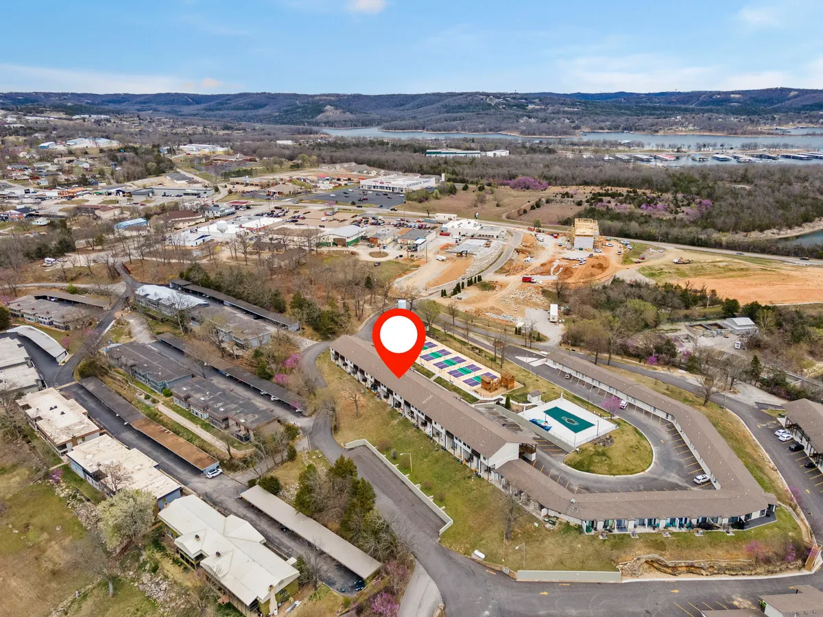 The exterior of a multi-story building with a sparkling swimming pool, landscaped greenery, and surrounding roads. The scene is vibrant and welcoming, with guests enjoying the outdoor amenities and communal atmosphere.