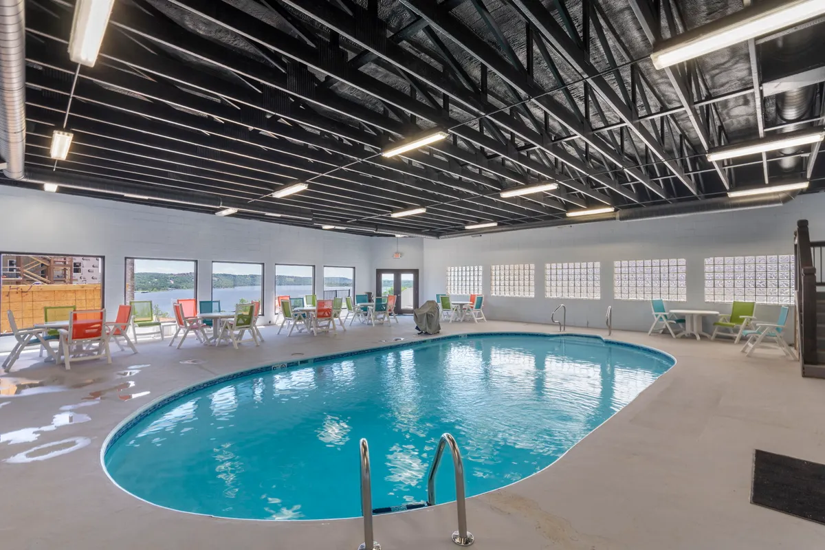 A bright, spacious indoor swimming pool area featuring colorful lounge chairs, large sunlit windows, and a sparkling pool perfect for year-round swimming and relaxation.