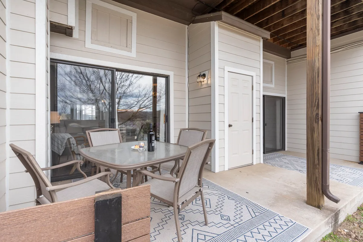 A stylish outdoor dining table and seating area set on a private patio, complete with a decorative rug and surrounded by subtle landscaping. The space is bathed in gentle sunlight, inviting guests to enjoy meals or relax outdoors.