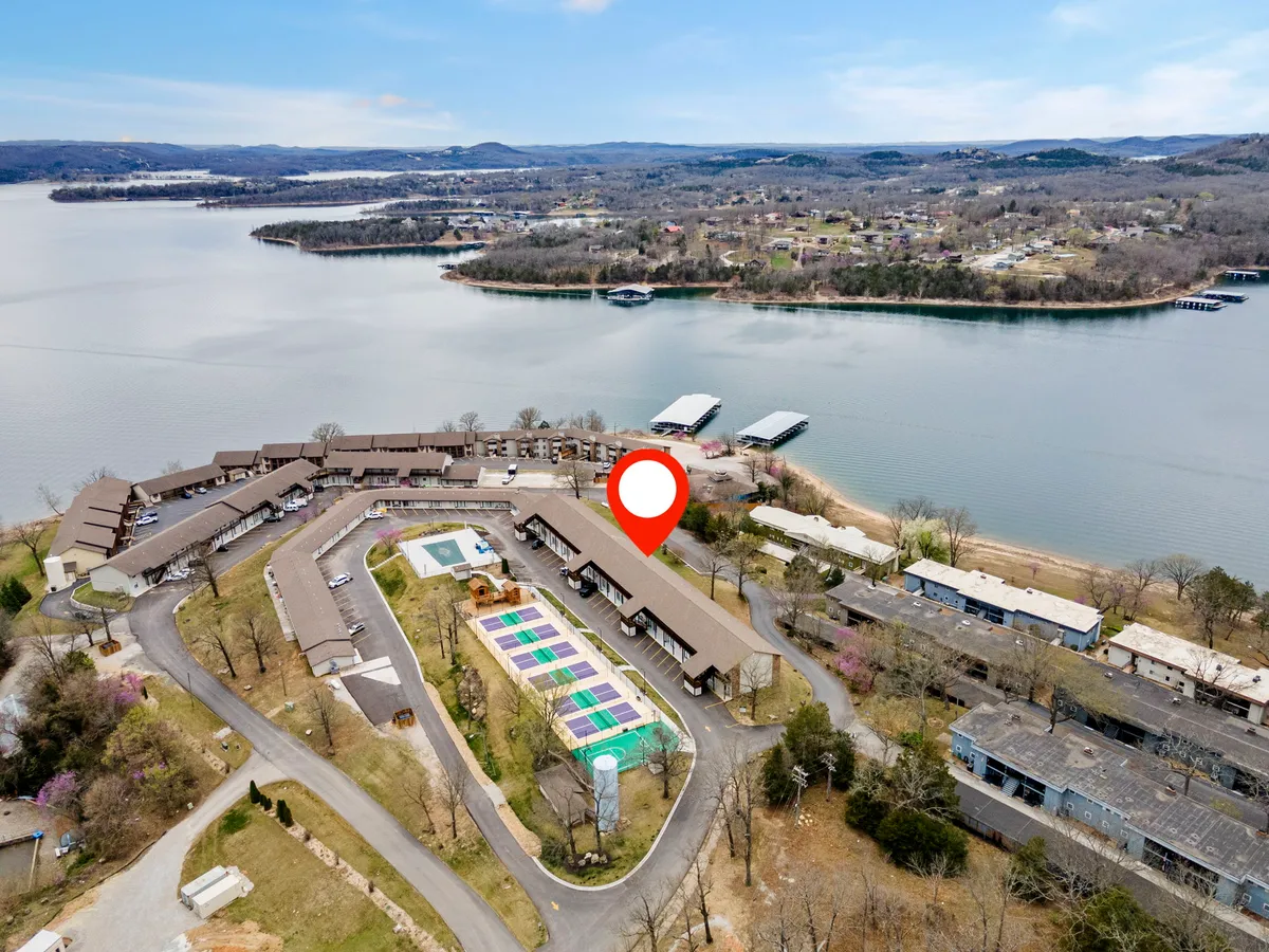 A vibrant exterior scene featuring Table Rock Lake in the background, a glistening swimming pool, and colorful sports courts surrounded by lush greenery. The image captures families enjoying water activities, picnicking, and playing sports.